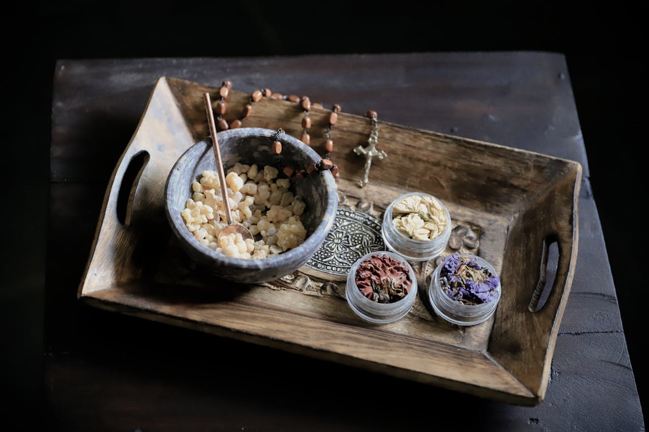 A rustic tray displaying incense, dried flowers, and a rosary evokes a calming, spiritual ambiance.
