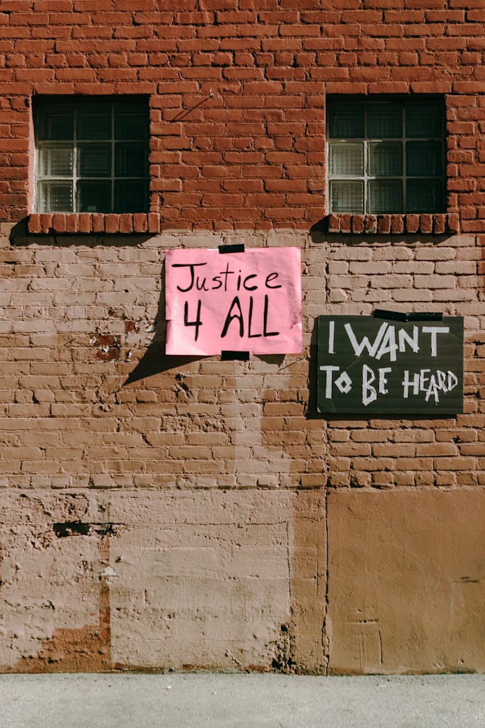 Street activism signs on a brick wall promoting social justice and freedom of speech.