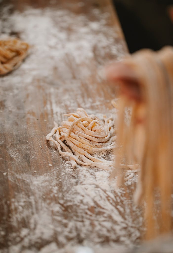 From above of crop anonymous blurred hand of female near table with flour and spaghetti